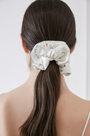 Woman showcasing the Princess Louise Silk Scrunchie with a floral design, tied in a ponytail.