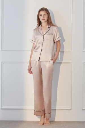 Model standing in blush pink MANITO Authentic Short Sleeve Pajama Set with black trim and soft satin texture.