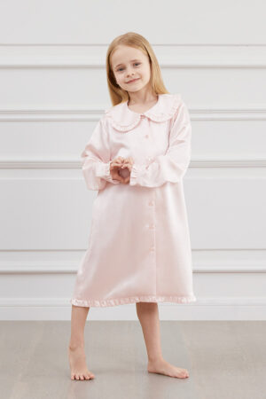 A girl in MANITO Pink Cloud Silk Nightgown with ruffled trim and pipped lapels.