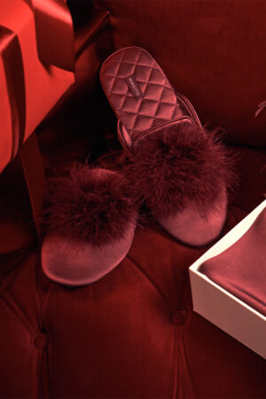 MANITO Silk Women's red slipper with feather accents, perfectly paired with a festive backdrop.