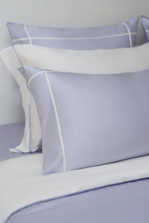 Close-up of MANITO Fluora Silk Bedding Set pillowcases with delicate white trim on soft lilac silk fabric.