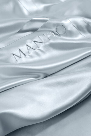 Luxurious MANITO 22 silk flat sheet with signature embroidery in a shimmering close-up, showcasing the elegant finish and craftsmanship.