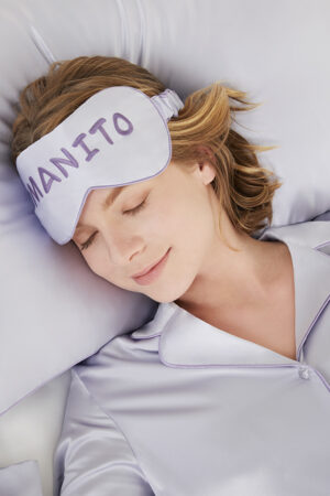 Woman sleeping peacefully wearing a MANITO macaron silk eye mask from the gift box, showcasing relaxation and comfort.