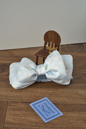 Close-up of blue MANITO DISNEY Alice Daisy Hair Band with daisy and Alice prints, styled with decorative props for a whimsical touch.