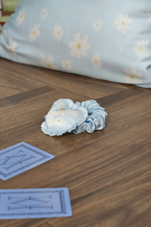 Blue MANITO Disney Alice Daisy Heart Hair Scrunchy placed on wooden floor showing a cozy lifestyle scene.