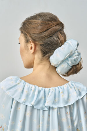 Side view of model styling hair with MANITO DISNEY Alice Daisy Puff Hair Scrunchy in blue silk.