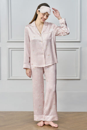 Smiling woman in pink MANITO DISNEY Daisy Pajama Set adjusting matching eye mask, capturing a cozy moment.