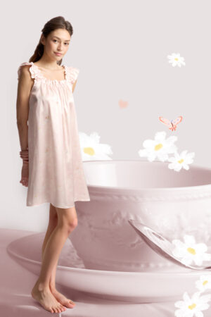 Woman in the pink MANITO Daisy Ruffle Nightdress standing barefoot beside an oversized teacup, surrounded by hand-drawn florals.