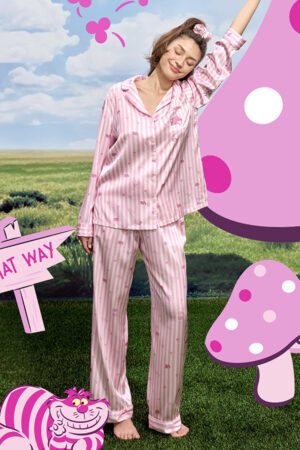 Model wearing MANITO DISNEY Cheshire Women's Pajama Gift Box in pink striped silk, stretching with eyes closed outdoors.