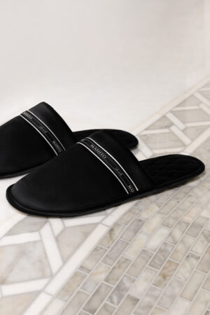 Black NoirRuban silk slippers set against patterned tiles, sleek slip-on profile and subtle shine from the satin finish.