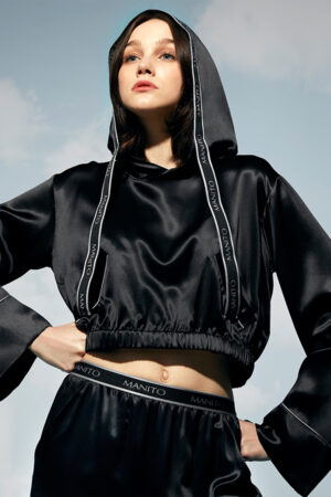 Woman gazing upward wearing a hooded Sportif Silk Tracksuit with branded trim detailing.