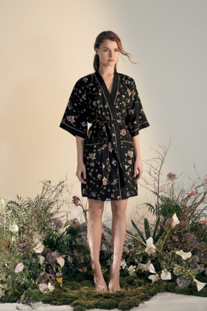 Woman in an simulated outdoor setting wearing a Lrisette Silk Short Kimono adorned with a floral pattern.