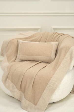 Sand Dune Knit Pillow and blanket styled on an armchair, creating a calm and cozy interior mood.