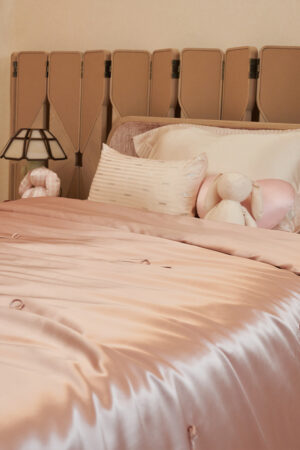Silk Throw Blanket in blush pink displayed on a neatly made bed with pillows and plush toys.