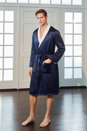 Model in navy MANITO silk terry cloth robe for men, with white shawl collar and belt, standing in front of French doors.