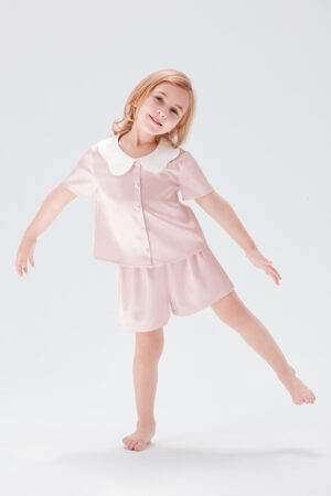 Little girl smiling in Doll Kid's Short Pajama Set with peter pan collar in ballet pink.