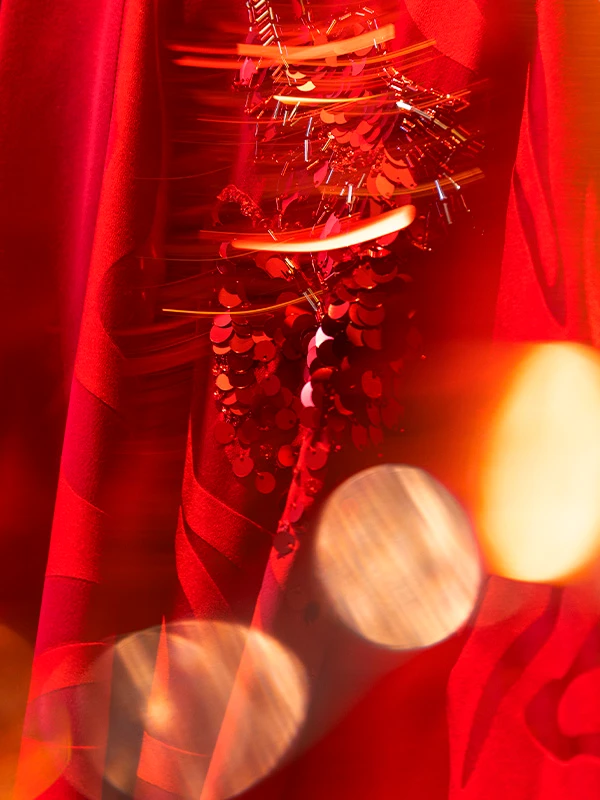 Red silk fabric with shimmering sequin embellishments under dramatic lighting.